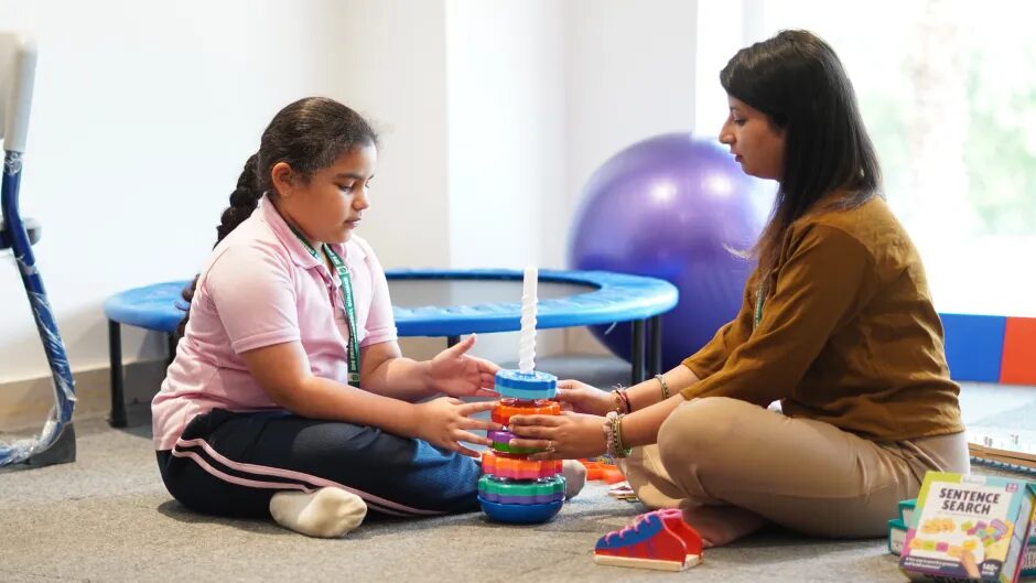 A therapist and a girl playing with a stacking toy on a mat