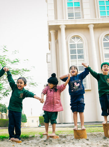 Young students in green uniforms playing on tree-stump steps outdoors